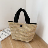 straw woven beach bag with black handles displayed on a wooden surface, perfect for summer outings.